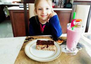 Dziewczynka siedzi przy stole. Przed dziewczynką deser na talerzu.
